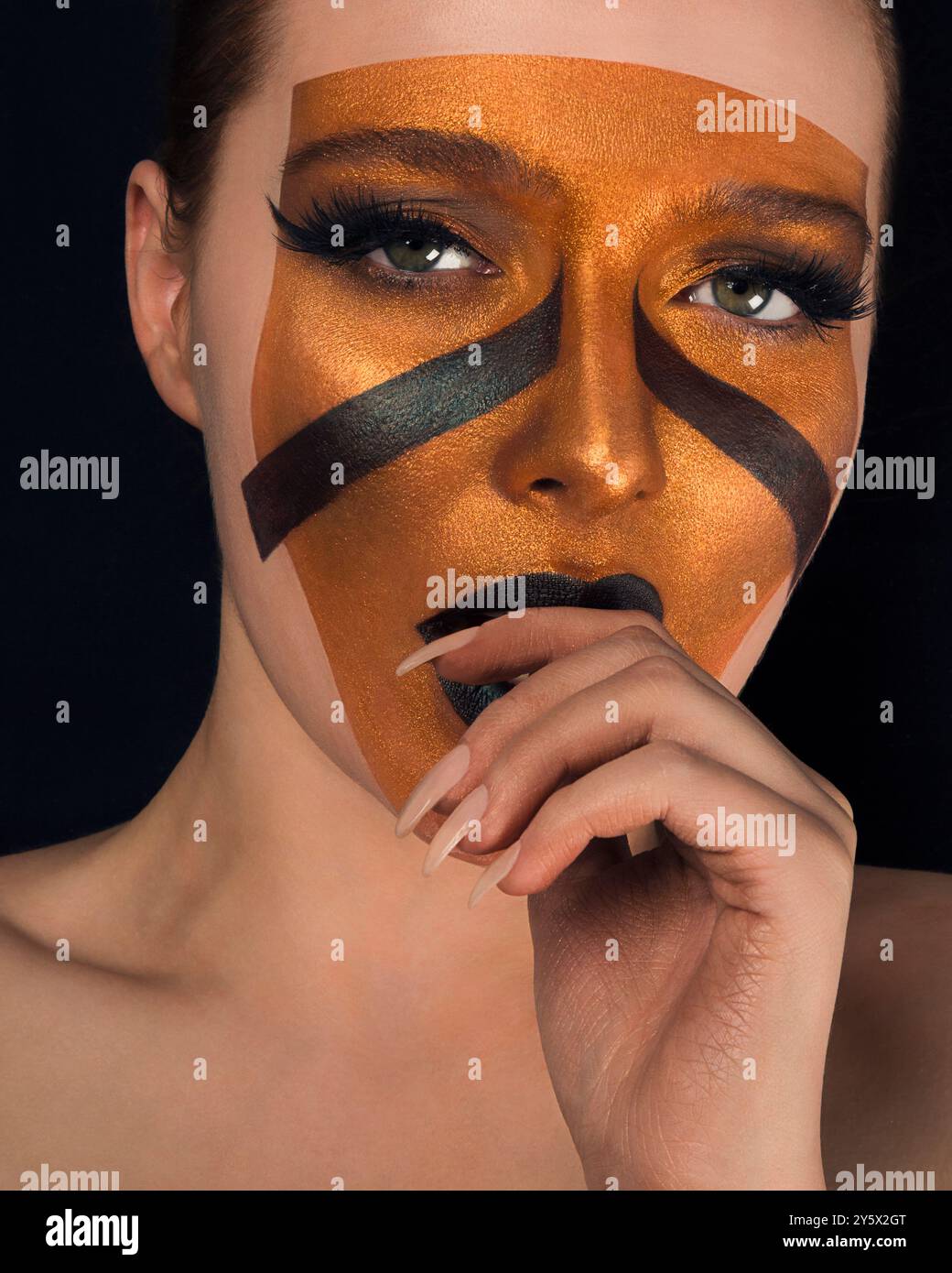 Nahaufnahme einer Frau mit auffälligem geometrischem Make-up-Design in Braun und Schwarz, das Gesicht und Augenlider bedeckt. Stockfoto