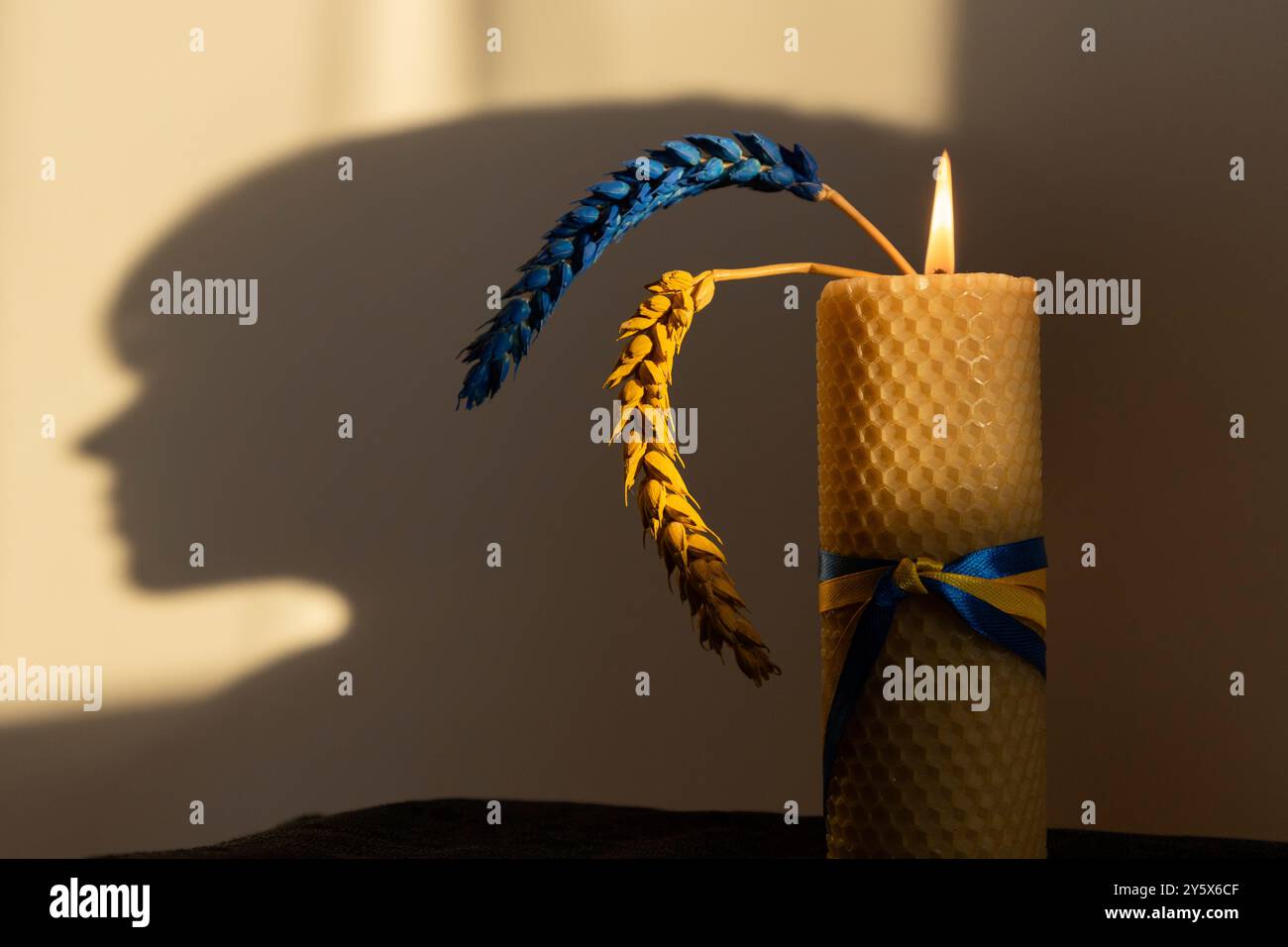 Brennende Kerze, zwei Weizenohren, gelb-blau vor dem Hintergrund des Schatten der Silhouette eines Kinderkopfes gemalt Stockfoto