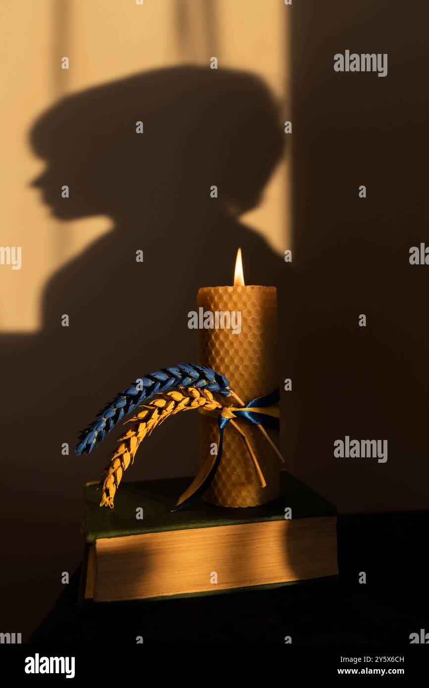 Brennende Kerze, zwei Spikelets, gelb-blau auf dunklem Hintergrund mit der Silhouette des Kinderkopfes Stockfoto