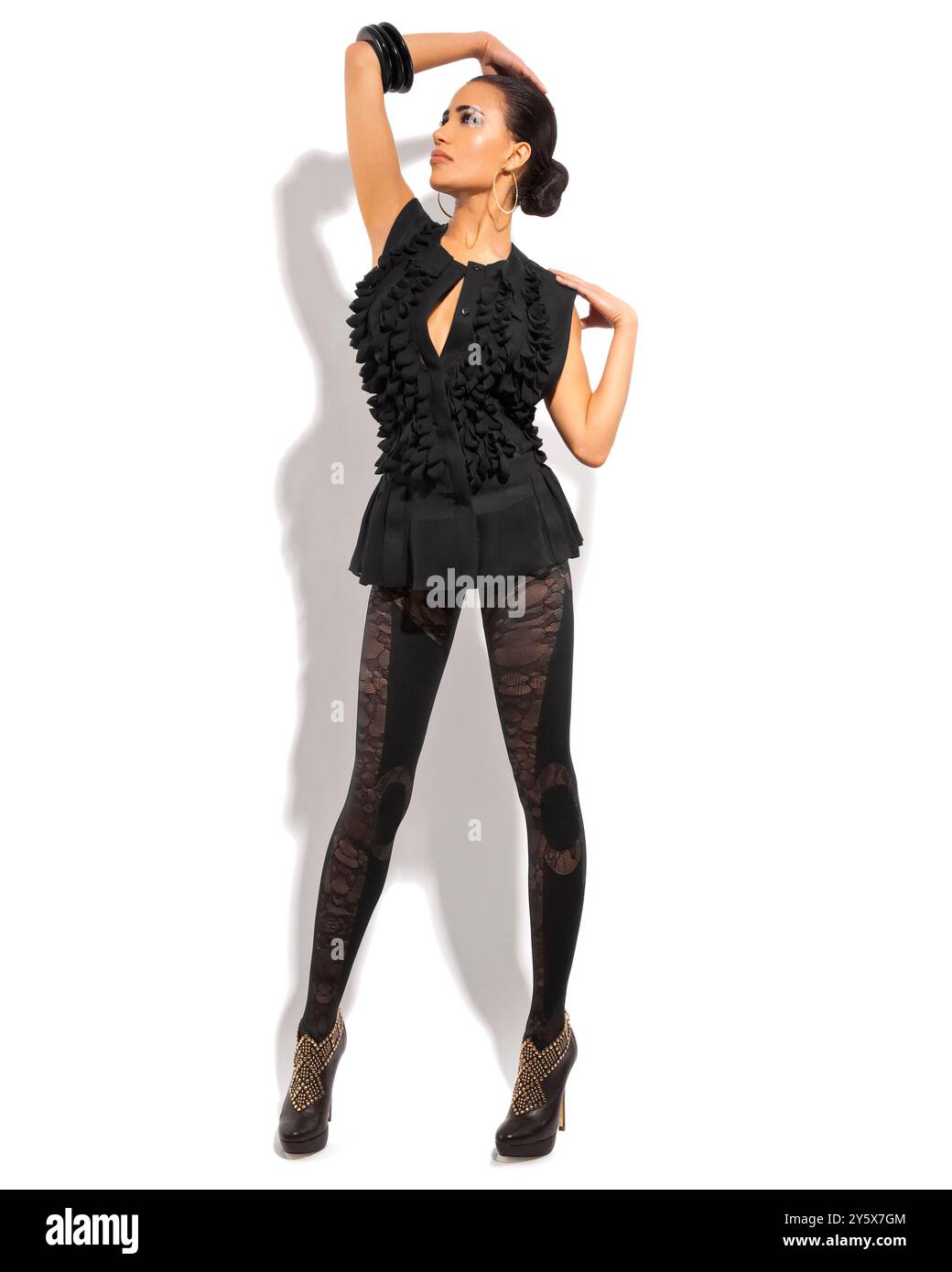 Modemodell posiert in einem stilvollen schwarzen Kleid vor weißem Hintergrund und wirft einen Schatten. Stockfoto