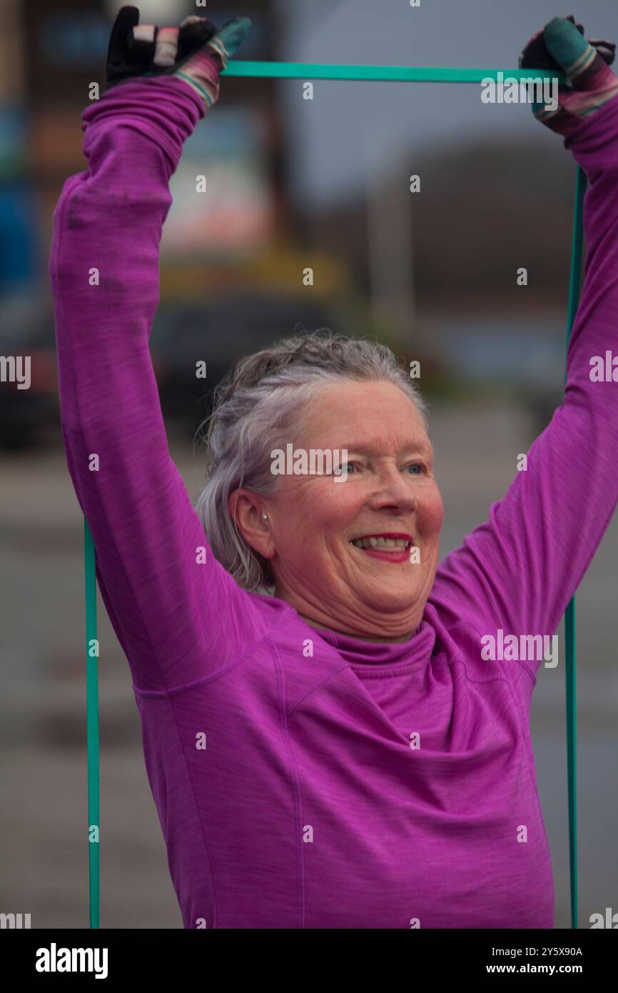 Ältere Frau, die im Freien mit einem Lächeln trainiert und Stretchbänder hält. Stockfoto