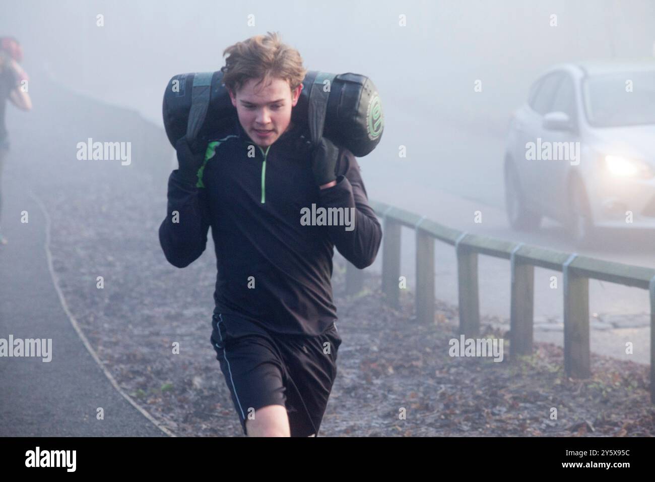 Junger Mann, der während eines Workouts mit schweren Sandsäcken auf einer nebeligen Straße läuft. Stockfoto