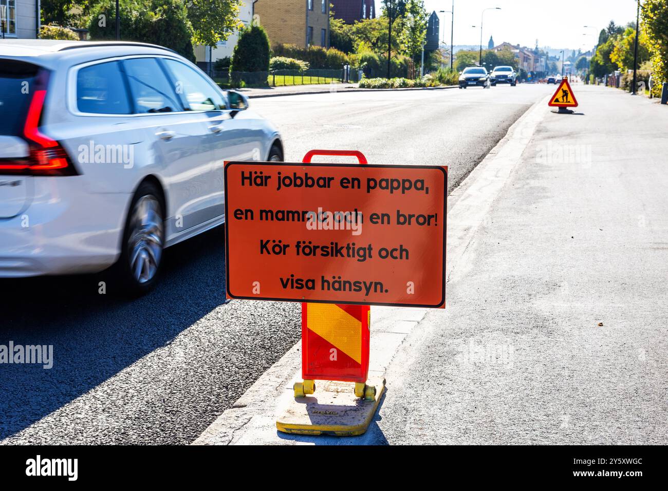 Informationen für Autofahrer, die während Bauarbeiten fahren. Hier ist ein Schild mit dem Text: Ein Vater, eine Mutter und ein Bruder arbeiten hier! Fahren Sie vorsichtig und seien Sie vorsichtig. (Auf schwedisch: Här jobbar en pappa, en mamma och en bror! KÖR försiktigt och Visa hänsyn). Stockfoto