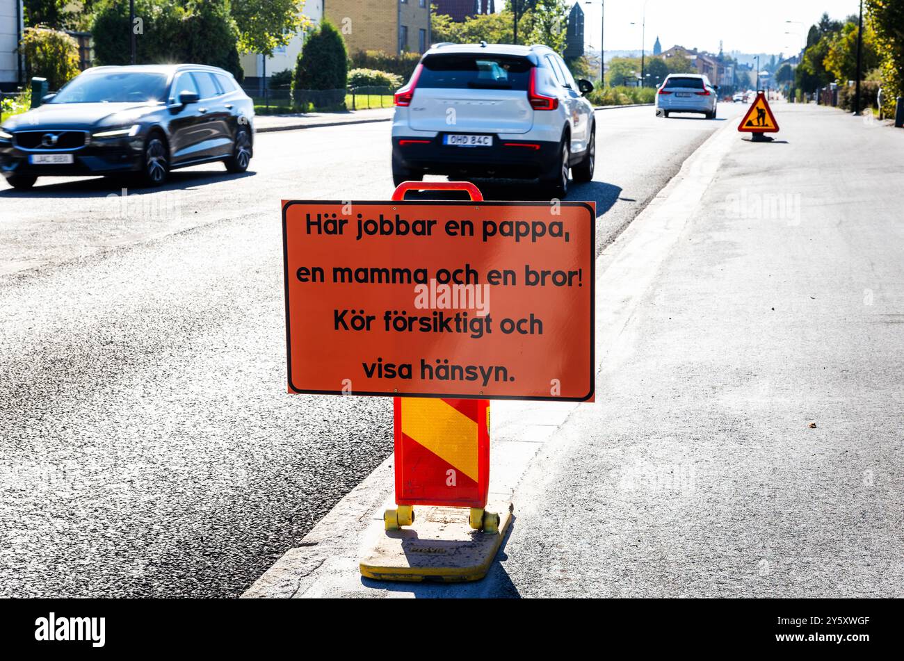 Informationen für Autofahrer, die während Bauarbeiten fahren. Hier ist ein Schild mit dem Text: Ein Vater, eine Mutter und ein Bruder arbeiten hier! Fahren Sie vorsichtig und seien Sie vorsichtig. (Auf schwedisch: Här jobbar en pappa, en mamma och en bror! KÖR försiktigt och Visa hänsyn). Stockfoto