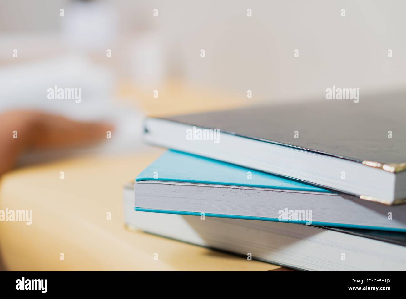 Ein Nahbild von drei gestapelten Büchern auf einem Holztisch, das eine ruhige Arbeitsumgebung mit sanfter natürlicher Beleuchtung perfekt einfängt. Ideal für den Unterricht Stockfoto