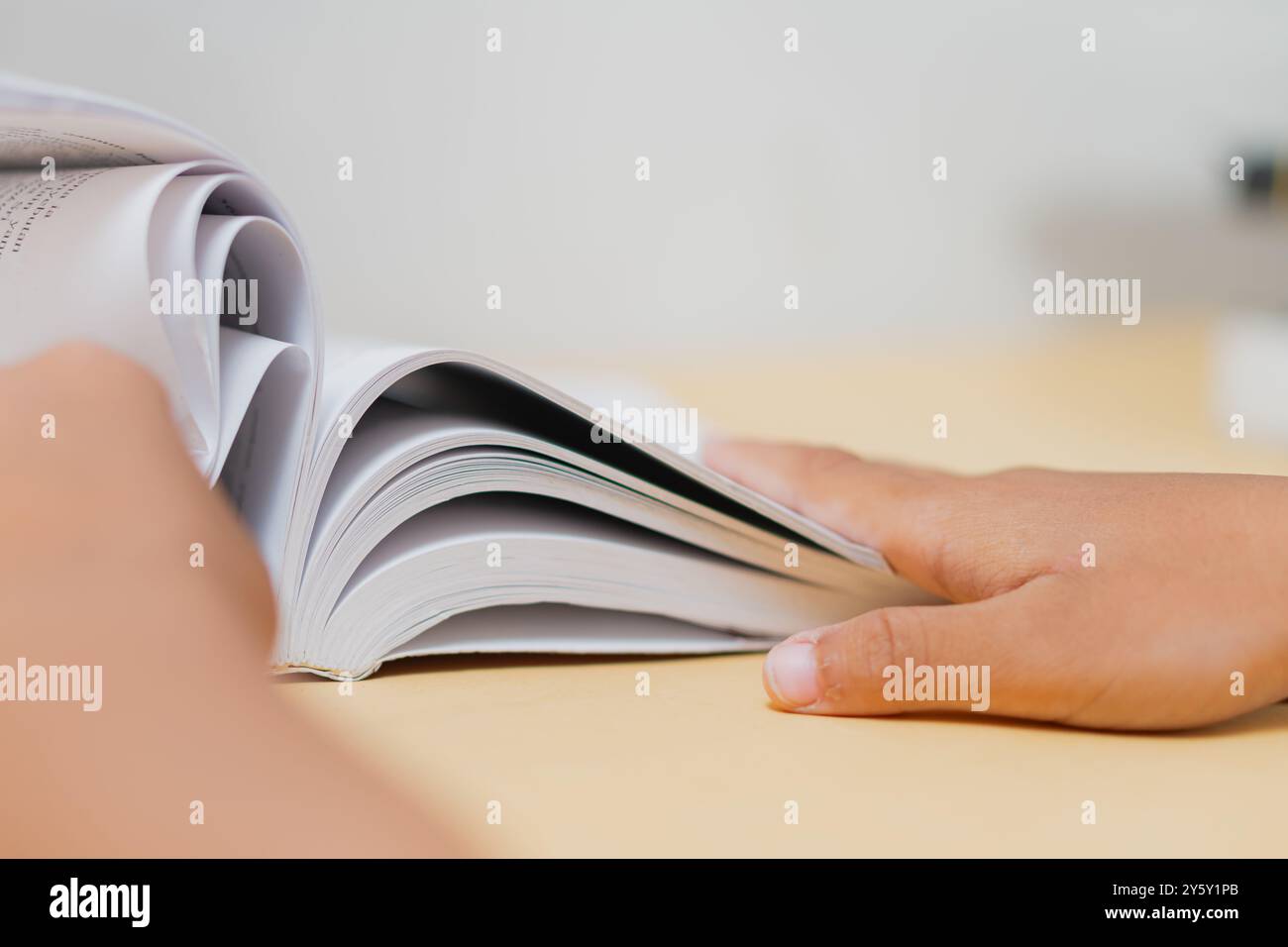 Nahaufnahme einer Person, die durch ein Buch auf einem Schreibtisch springt und dabei das Konzept des Lesens, der Konzentration und des Lernens in einer ruhigen Umgebung festlegt. Stockfoto