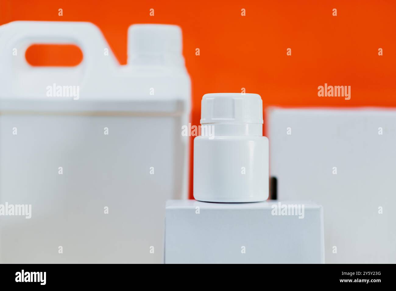 Nahaufnahme von weißen Kunststoffbehältern vor einem leuchtend orangefarbenen Hintergrund, die Verpackung und Produktdesign betonen. Geeignet für Themen rela Stockfoto