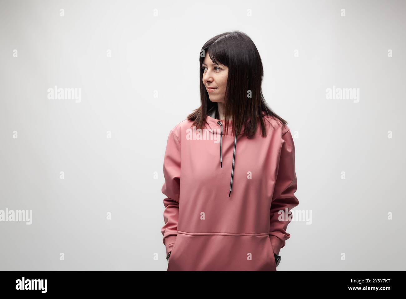 Eine nachdenkliche junge Frau in einem lässigen rosafarbenen Hoodie schaut zur Seite, dargestellt vor einem weichen grauen Hintergrund, was ein Gefühl der Besinnung weckt. Stockfoto