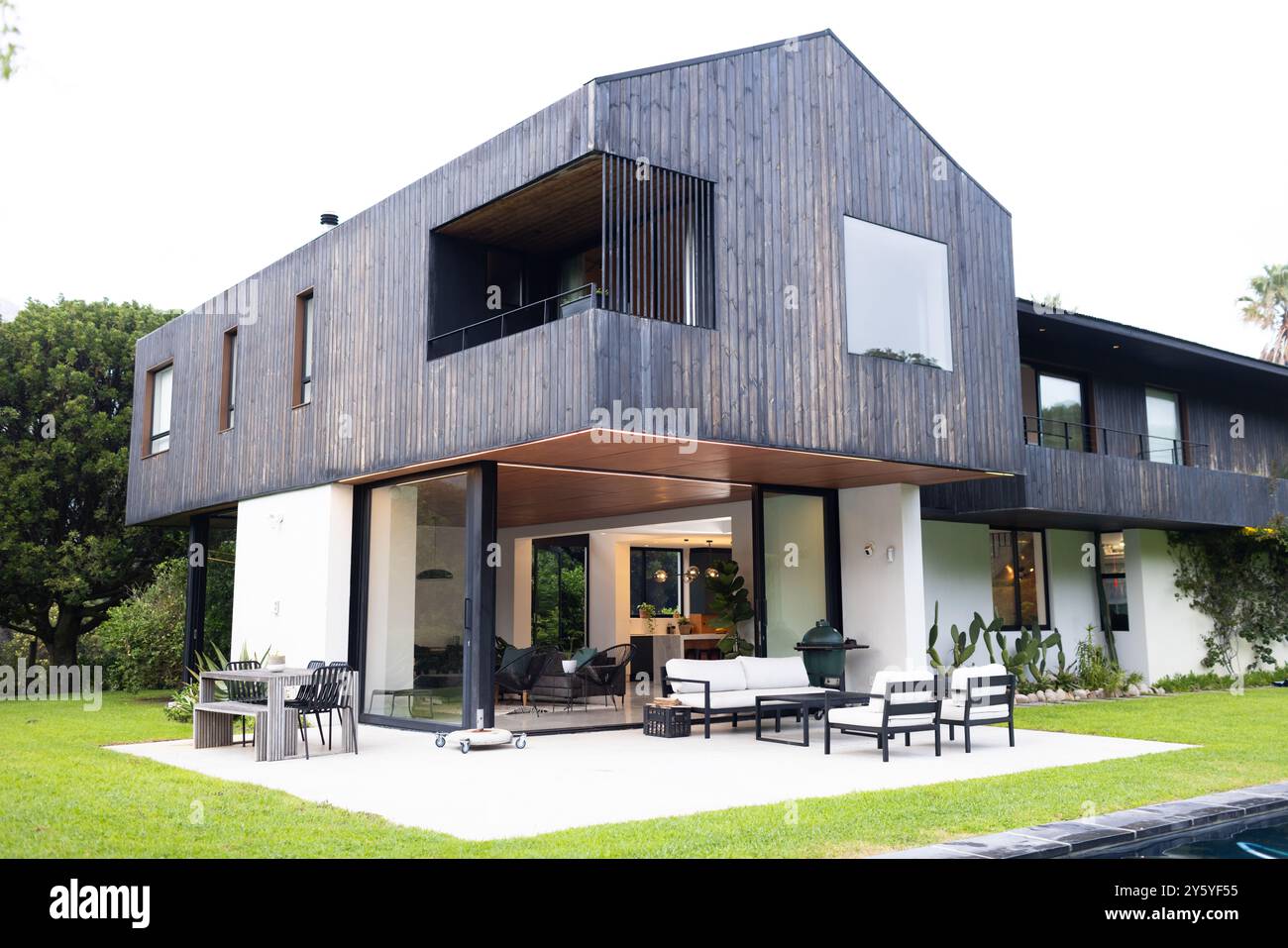 Modernes Haus mit großen Fenstern und Sitzbereich im Freien auf grünem Rasen, Kopierraum Stockfoto