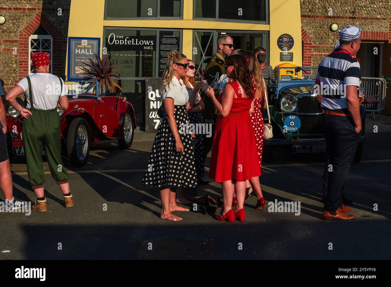 Sheringham, Norfolk, Großbritannien - 21. SEPTEMBER 2024: Gruppe der Frauen in 1940er Jahren gekleidet Vintage-rote und schwarze Kleider sprechen Stockfoto