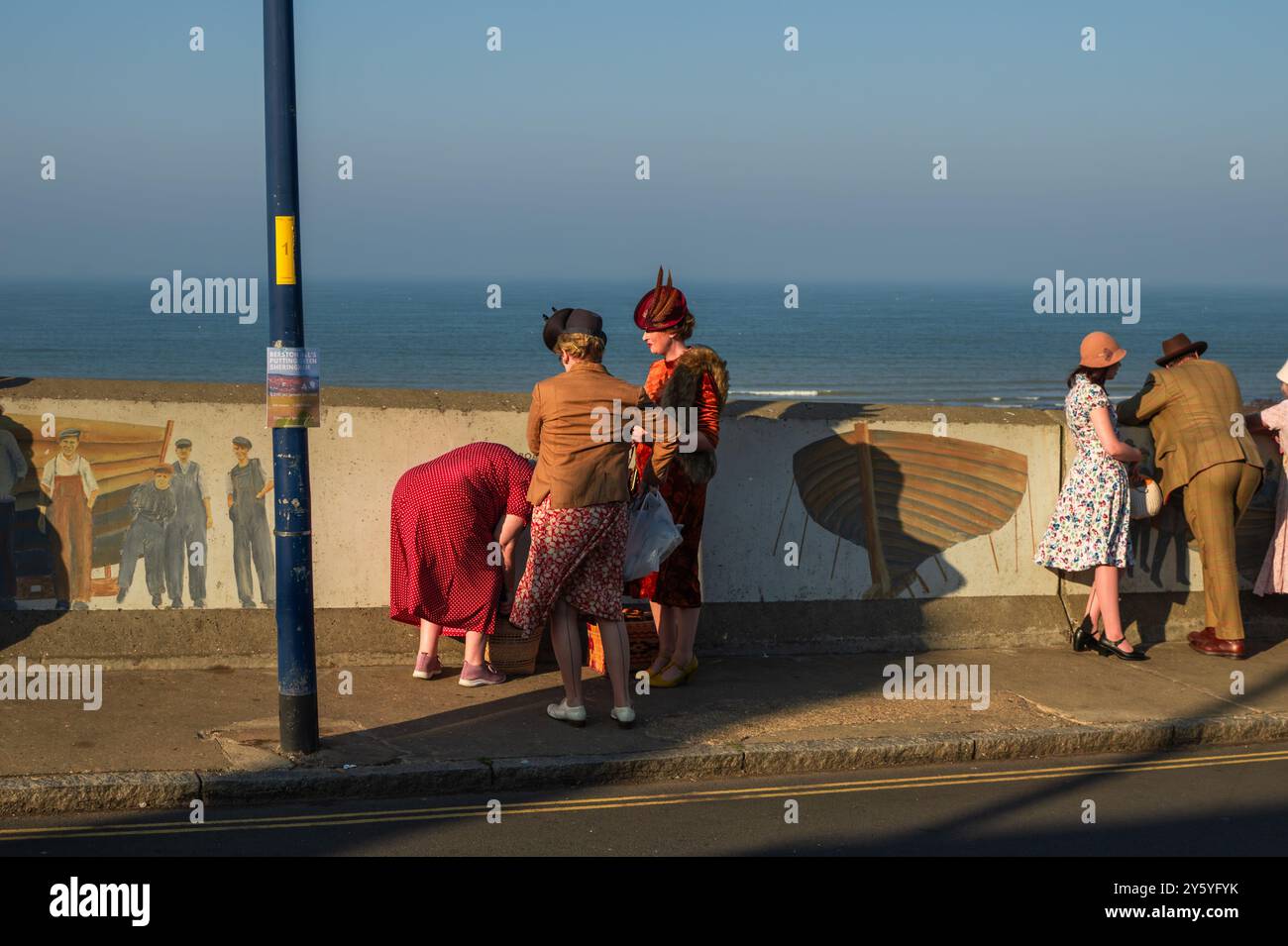 Sheringham, Norfolk, Großbritannien - 21. SEPTEMBER 2024: Frauen in Vintage-Kleidern der 1940er Jahre neben der Wand mit Blick auf das Meer Stockfoto
