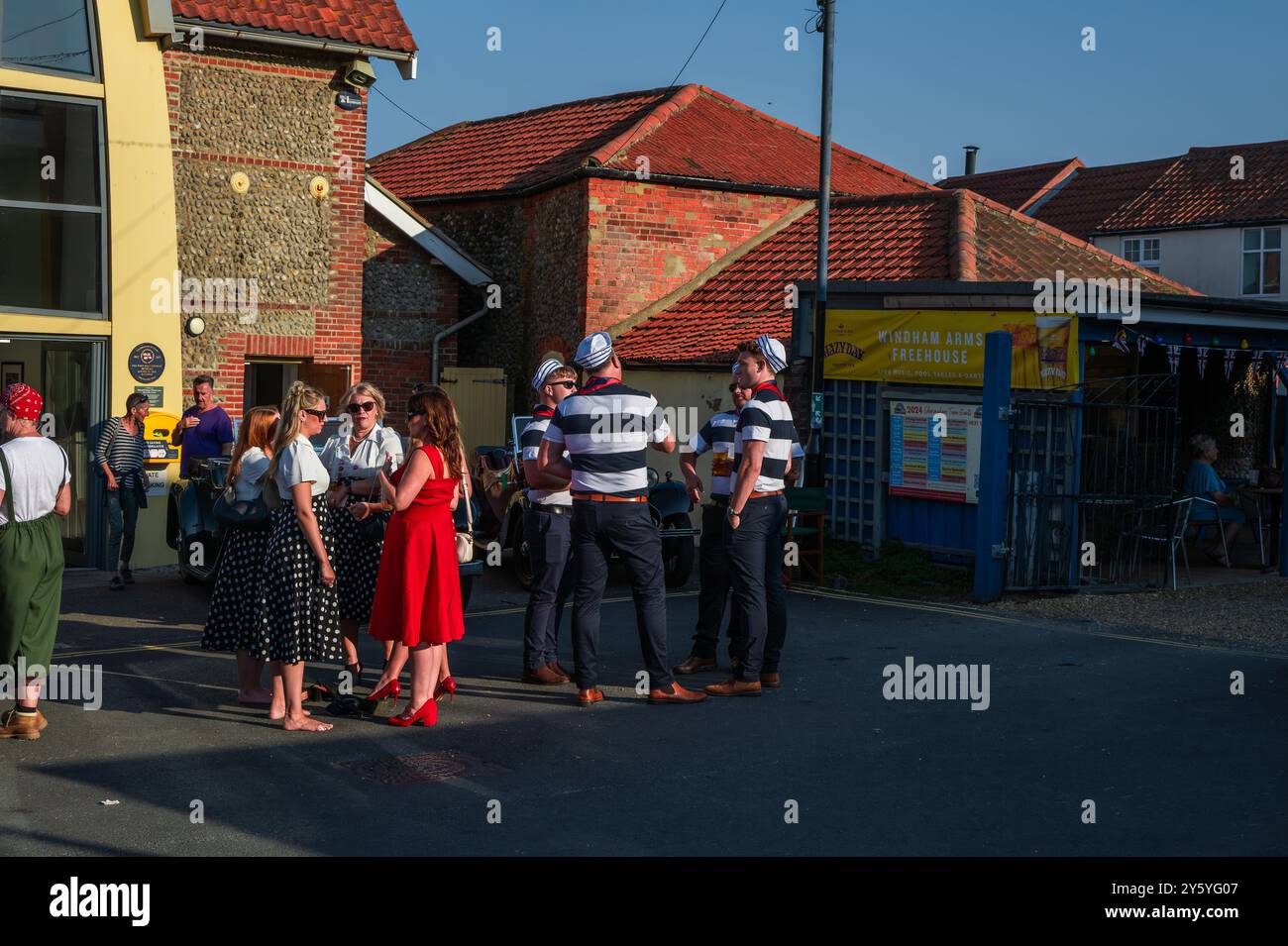 Sheringham, Norfolk, Großbritannien - 21. SEPTEMBER 2024: Gruppe der Frauen in Vintage-Kleidern der 1940er Jahre und Gruppe von Matrosen im Gespräch Stockfoto