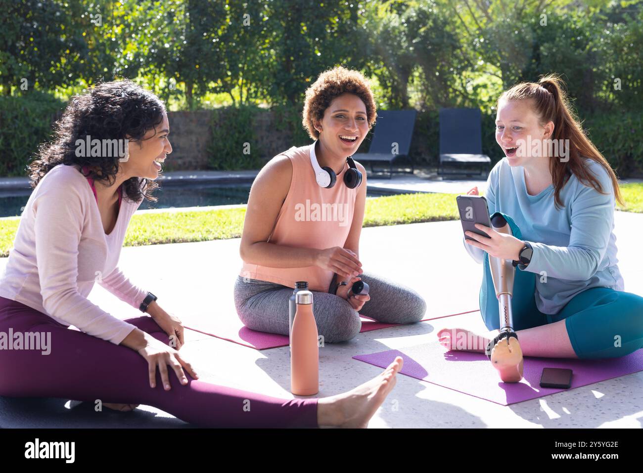 Sitzen auf Yogamatten, verschiedene Freundinnen plaudern und lachen draußen Stockfoto