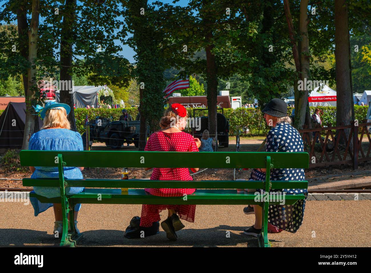 Holt, Norfolk, Großbritannien - 21. SEPTEMBER 2024: Foto von Frauen in eleganten blauen, schwarzen und blauen Vintage-Kleidern der 1940er Jahre, die während des Wochenendes der 1940er Jahre auf der Bank sitzen Stockfoto
