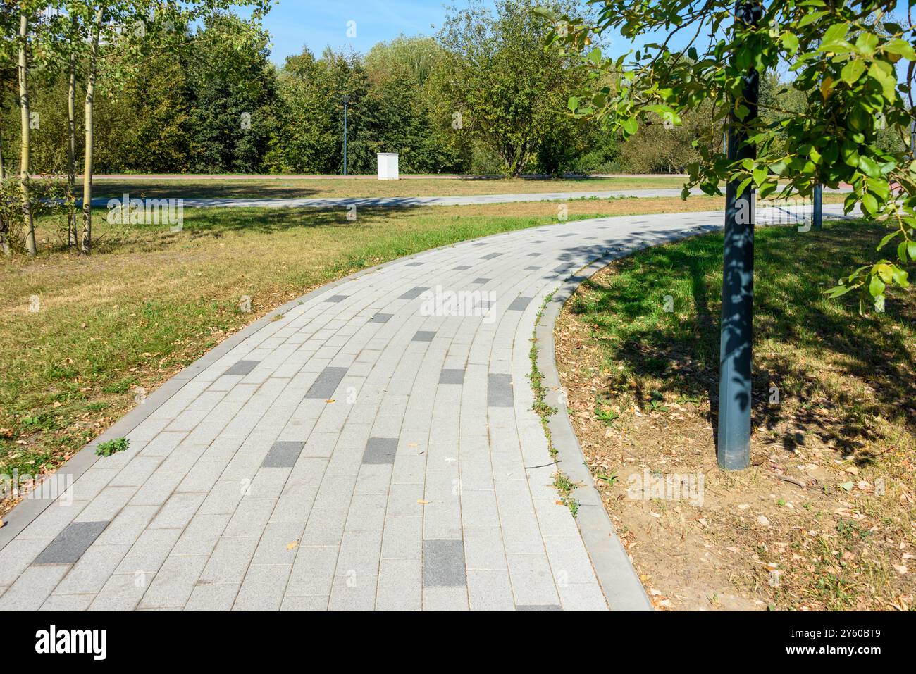 Ein Fußgängerweg aus Pflasterplatten vor dem Hintergrund eines gepflegten Rasens. Ein Spaziergang im Park. Stockfoto