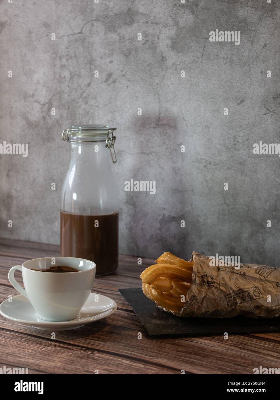 Vertikales Foto einer Tasse heiße Schokolade mit Churros auf Schiefer und Holztisch Stockfoto