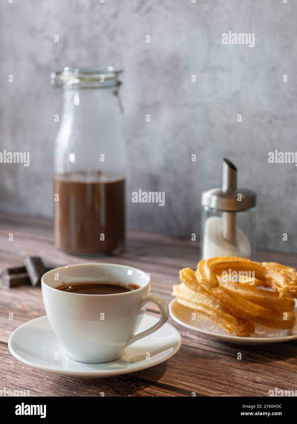 Vertikales Foto eines warmen Schokoladenfrühstücks in einer Tasse mit Churros. Glasflasche mit Schokolade unten. Stockfoto