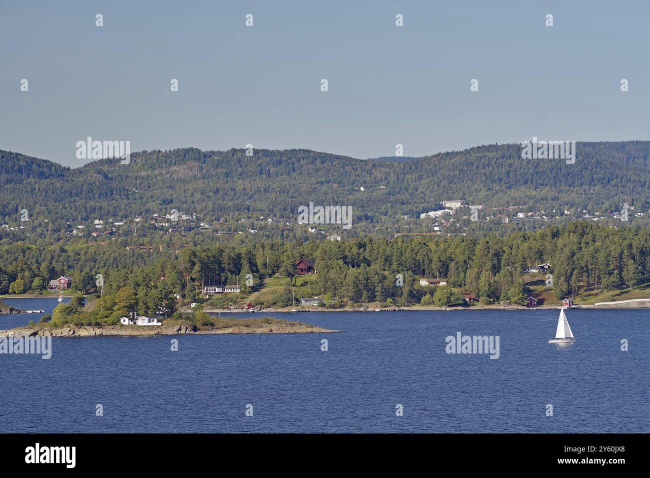Ein einsames Segelboot in der Nähe einer kleinen Insel, umgeben von Wasser und bewaldeten Hügeln im Hintergrund, Oslofjord, Hauptstadt, Oslo, Norwegen, Europa Stockfoto