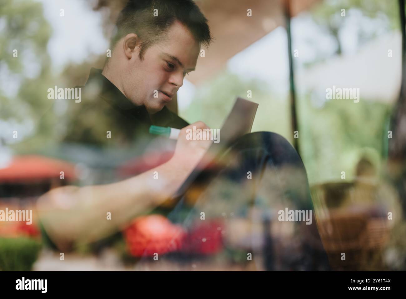 Junger Mann mit Down-Syndrom, der in ein Notizbuch schreibt Stockfoto