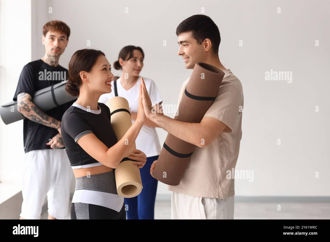 Sportliche Jugendliche mit Yogamatten, die sich gegenseitig High-Five im Fitnessstudio geben Stockfoto