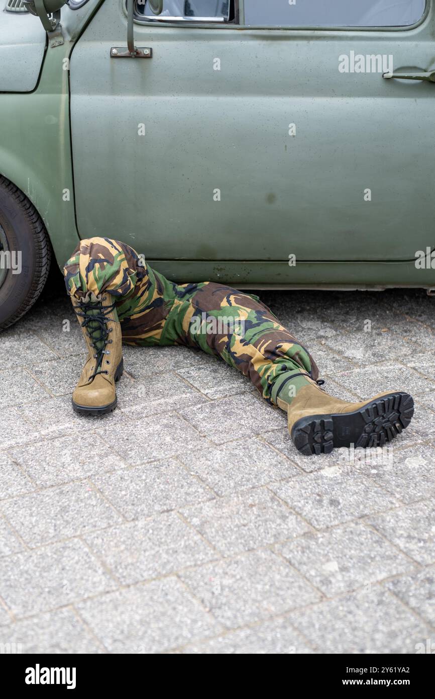 Militärmechaniker in Tarnung, der unter einem alten Fahrzeug arbeitet. Die Szene erfasst das Wesen der Wartung und Reparatur vor Ort in einem realistischen Outdo Stockfoto