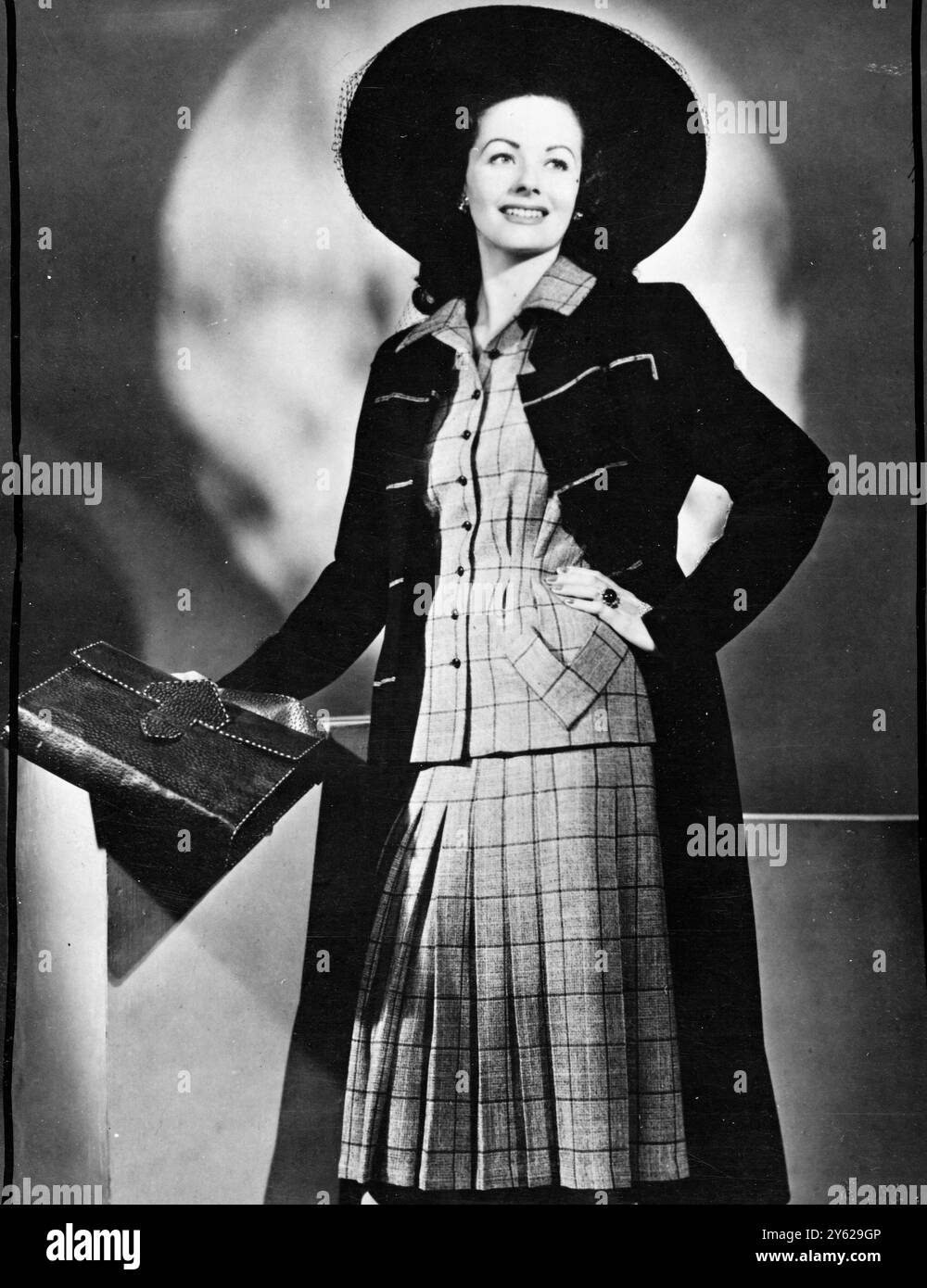 Margaret Lockwood, der junge Star der J. Arthur Rank-Organisation, nimmt sich in diesem vom Wachmann inspirierten Mantel aus marineblauer Wolle mit einer Militärmischung an. Der kurzärmelige Anzug in grauen, marineblauen und roten Tweed hat einen ausgestellten Rock und die Jacke ist an der Taille gerafft und unterstreicht den Hüftbereich. Joy Ricardo hat das atemberaubende Ensemble für die First Lady der britischen Filme geschaffen. 24. Dezember 1947 Stockfoto