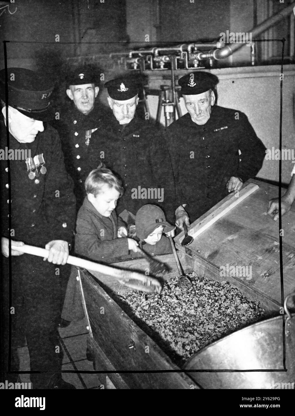 Eifrig als Schuljungen für ihren Weihnachtspudding sind die galanten alten Rentner des Chelsea Royal Hospital, und die Zeremonie des Mischens des traditionellen Gerichts wird mit gebührender Hochachtung beobachtet. All die guten Dinge, die normalerweise in Weihnachtspuddings zu finden sind, werden mit einer Ausnahme berücksichtigt, da ein aufgeregter Rentner vor 20 Jahren eine Münze verschluckt hat, wird es in Chelsea-Puddings keine Sechsecken geben. Das Bild zeigt: Von links nach rechts, der 75-jährige Sapper Harry Kybett aus Rochester, rührt die Pudding-Mischung mit Unterstützung des sechsjährigen Francis Witts, Sohn des Vizegouverneurs des Krankenhauses und Fou Stockfoto