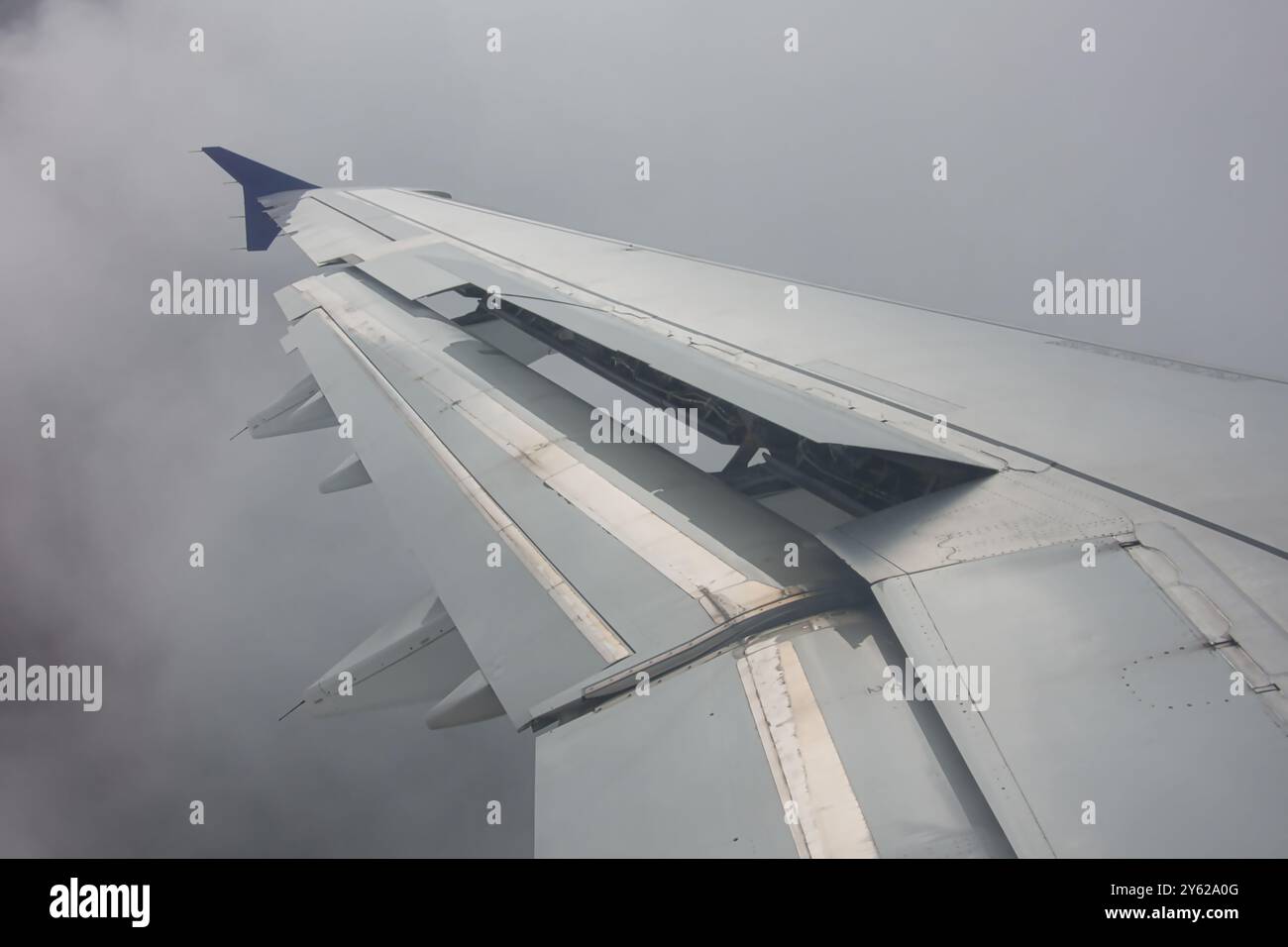 Nahaufnahme eines Flugzeugflügels mit verlängerten Laschen in dichtem Nebel, Flugverkehr über den Wolken. Stockfoto