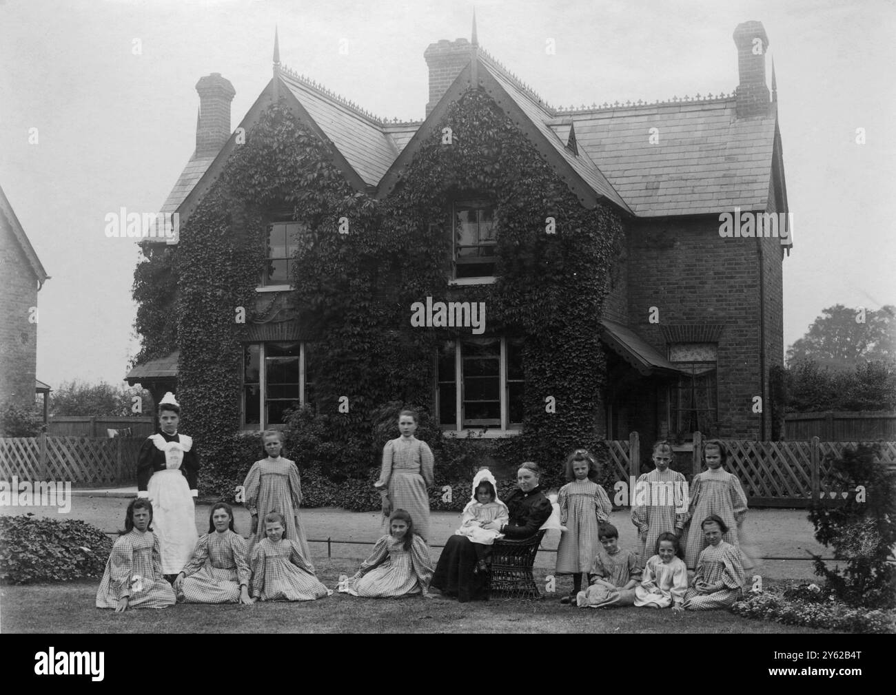 ARCHIV BOX 6 ARC 0189 REFERENZ: 001488 MÄDCHEN DORF HAUS : GRUPPE UND HÜTTE DATUM: C 1895 GRUPPE VON MÄDCHEN UND PERSONAL VOR EINEM FERIENHAUS AUF DEM ERSTEN GRÜN Stockfoto