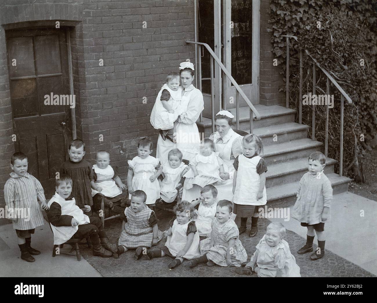 ARCHIV BOX 2 ARC 0046 D149 ARC REFERENZ: SCHLOSS 001343 BABYS : KRANKENSCHWESTERN UND SÄUGLINGE DATUM: C 1890 ZWEI KRANKENSCHWESTERN MIT 15 SÄUGLINGEN : KRANKENSCHWESTERN IN UNIFORM : JUNGEN IN KLEIDERN Hawkhurst Castle Cranbrook Road , Hawkhurst , Kent , England Stockfoto