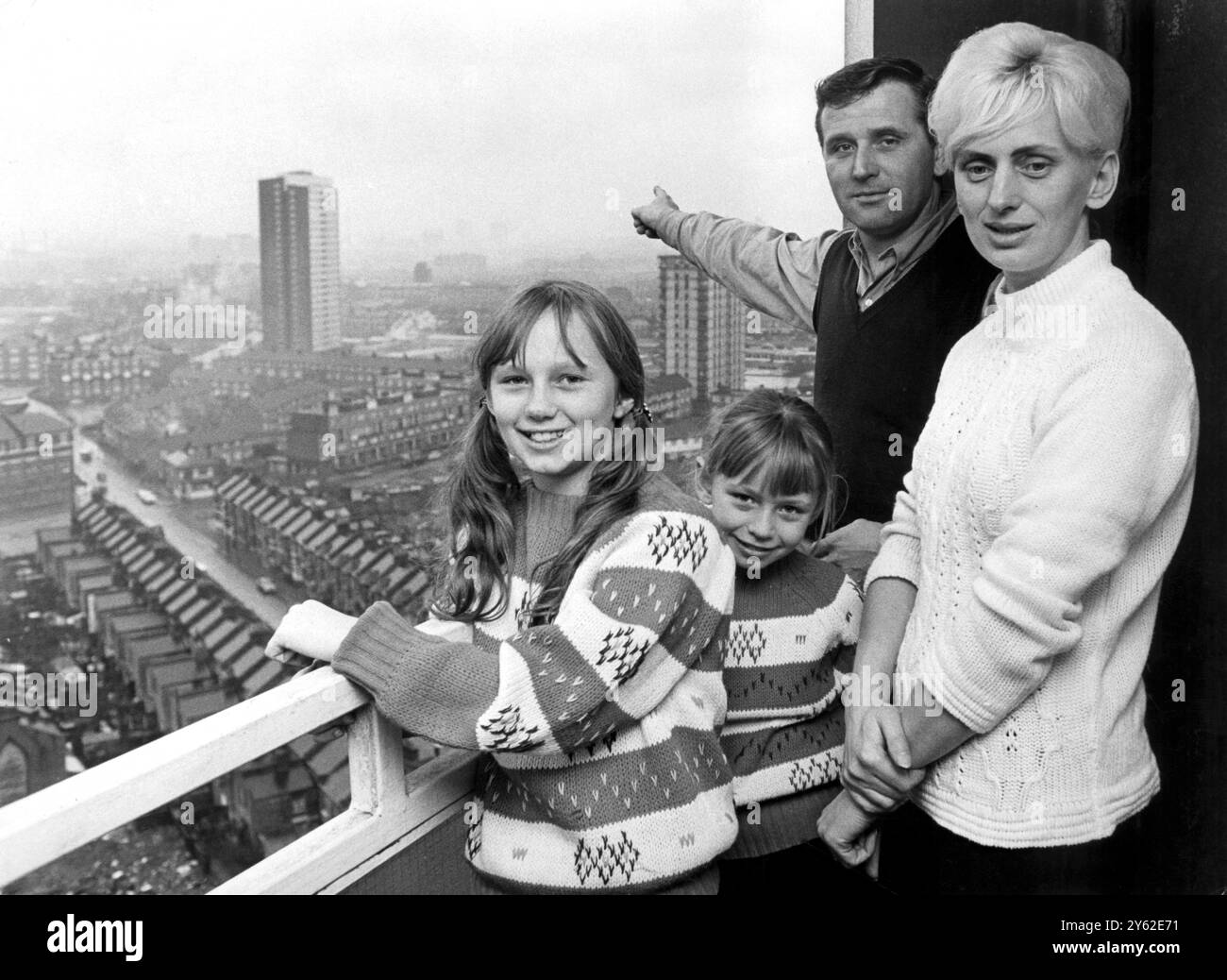 Eine Familie "am Himmel", die nicht mehr unter einer Wolke der Angst leben wird, falls der Wohnblock, in dem sie lebten, zusammenbrechen sollte. Sie sind Herr Graham und Frau Ingeburg Payne mit den Kindern Diana (7) und Susan (11). Herr Payne weist auf den neuen Block traditioneller Wohnungen hin, Ferrier Point, der im linken Hintergrund zu sehen ist, in den sie verschoben wurden, kurz nachdem dieses Bild am Merritt Point aufgenommen wurde, einem Systemblock im Londoner Stadtteil Newham. Die Paynes gehörten zu den ersten von 115 Familien, die ausgezogen wurden, damit die systemgebauten Blöcke verstärkt werden konnten, um Certai herzustellen Stockfoto