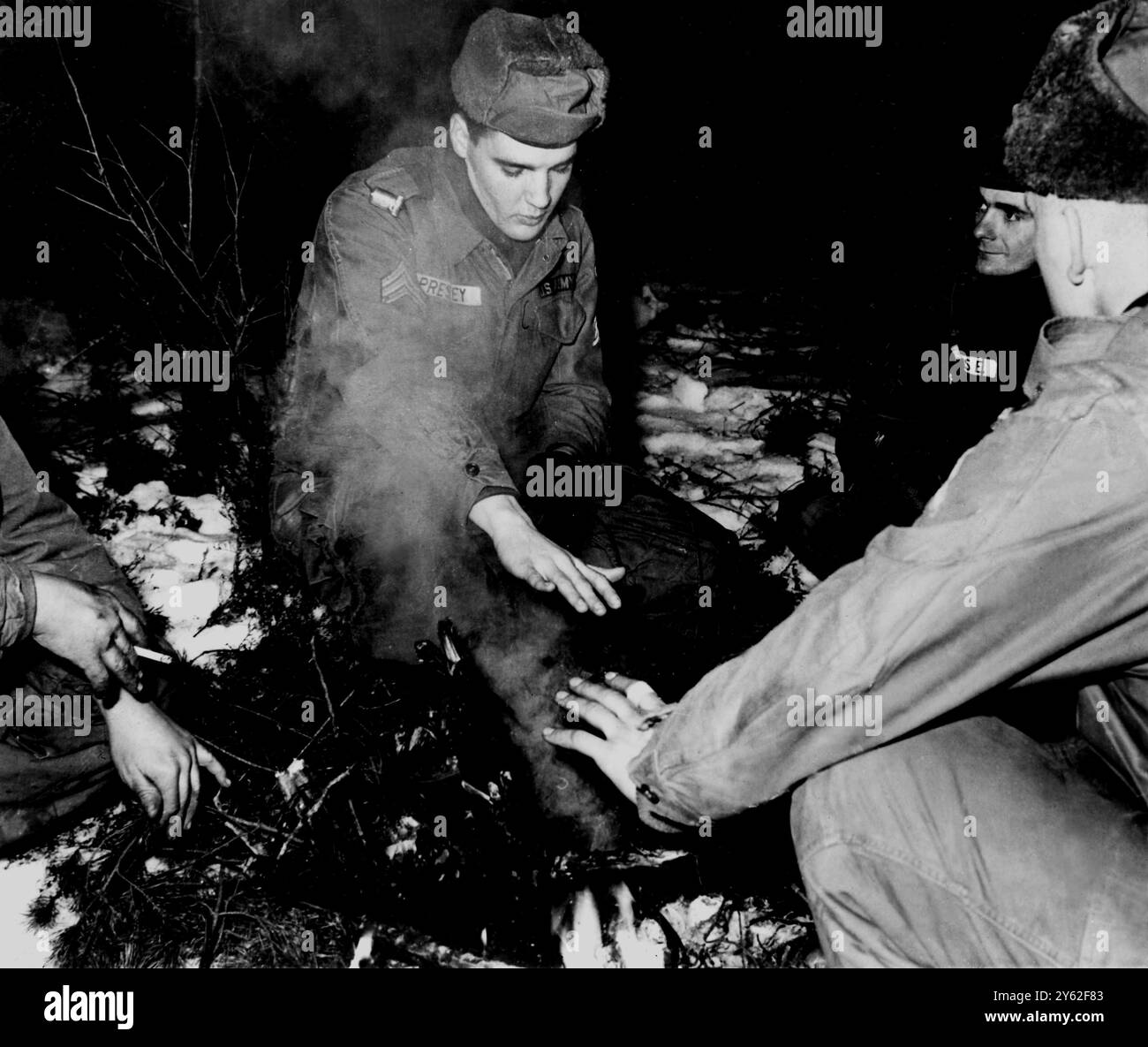 8. Februar 1960: Grafenwoeur, Bundesrepublik Deutschland. Rock n rll-Sänger Elvis Presley, jetzt ein kommissarischer Sergeant in der US-Armee, wärmt seine Hände bei einem rauchigen Feuer in seiner letzten Nacht voller Manöver. Er wird nach zwei Jahren im National Service in die Vereinigten Staaten zurückkehren, um seine Karriere als Gesangsspieler fortzusetzen. UPI Stockfoto 8. Februar 1960: Grafenwoeur, Bundesrepublik Deutschland. Rock n rll-Sänger Elvis Presley, jetzt ein kommissarischer Sergeant in der US-Armee, wärmt seine Hände bei einem rauchigen Feuer in seiner letzten Nacht voller Manöver. Er wird nach zwei Jahren im National Service in die Vereinigten Staaten zurückkehren, um seine Karriere als Gesangsspieler fortzusetzen. UPI Stockfoto