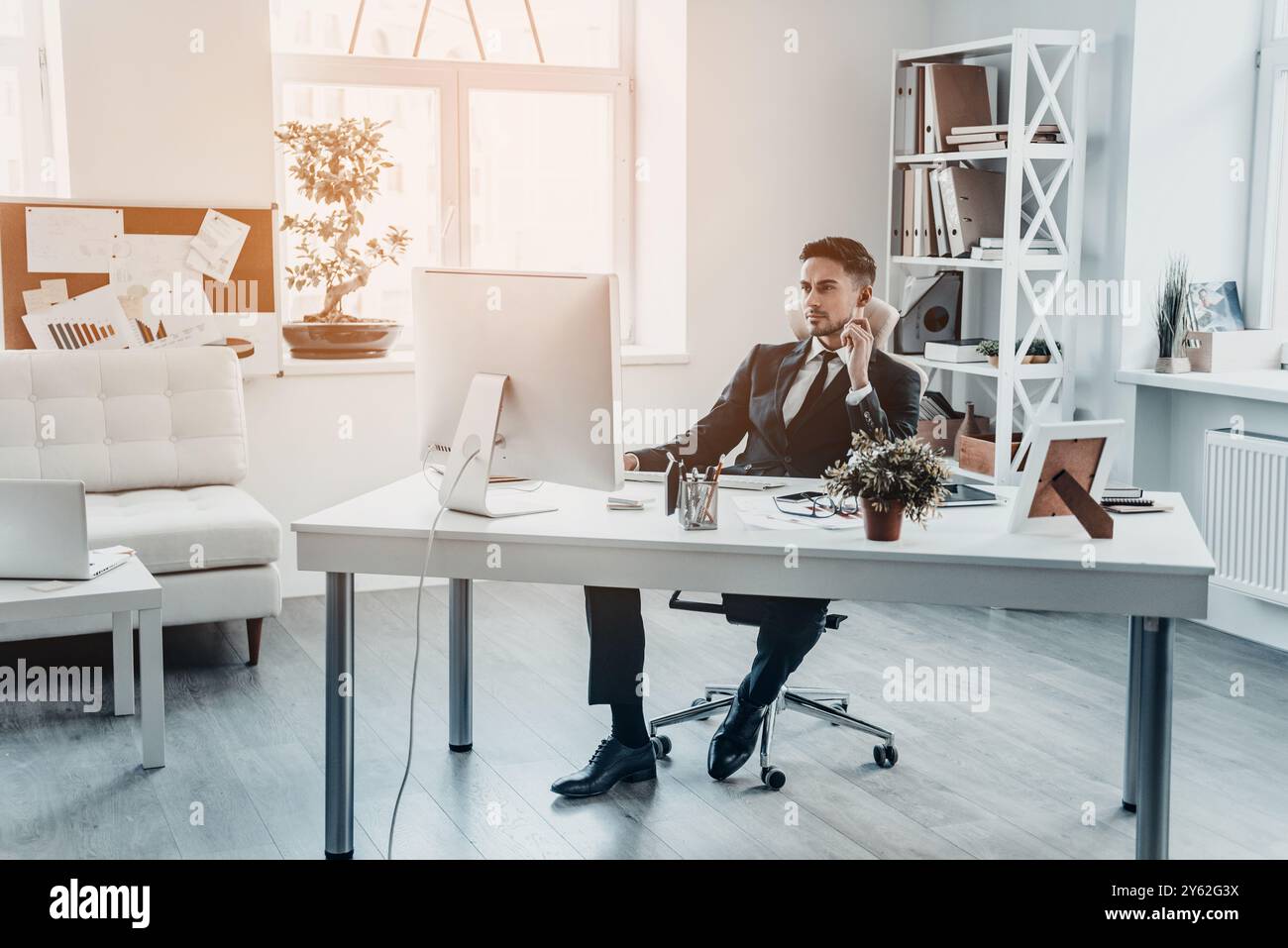 Über neue Lösungen nachdenken. Hübscher junger Mann in formeller Kleidung, der auf den Computermonitor blickt, während er am Schreibtisch sitzt Stockfoto