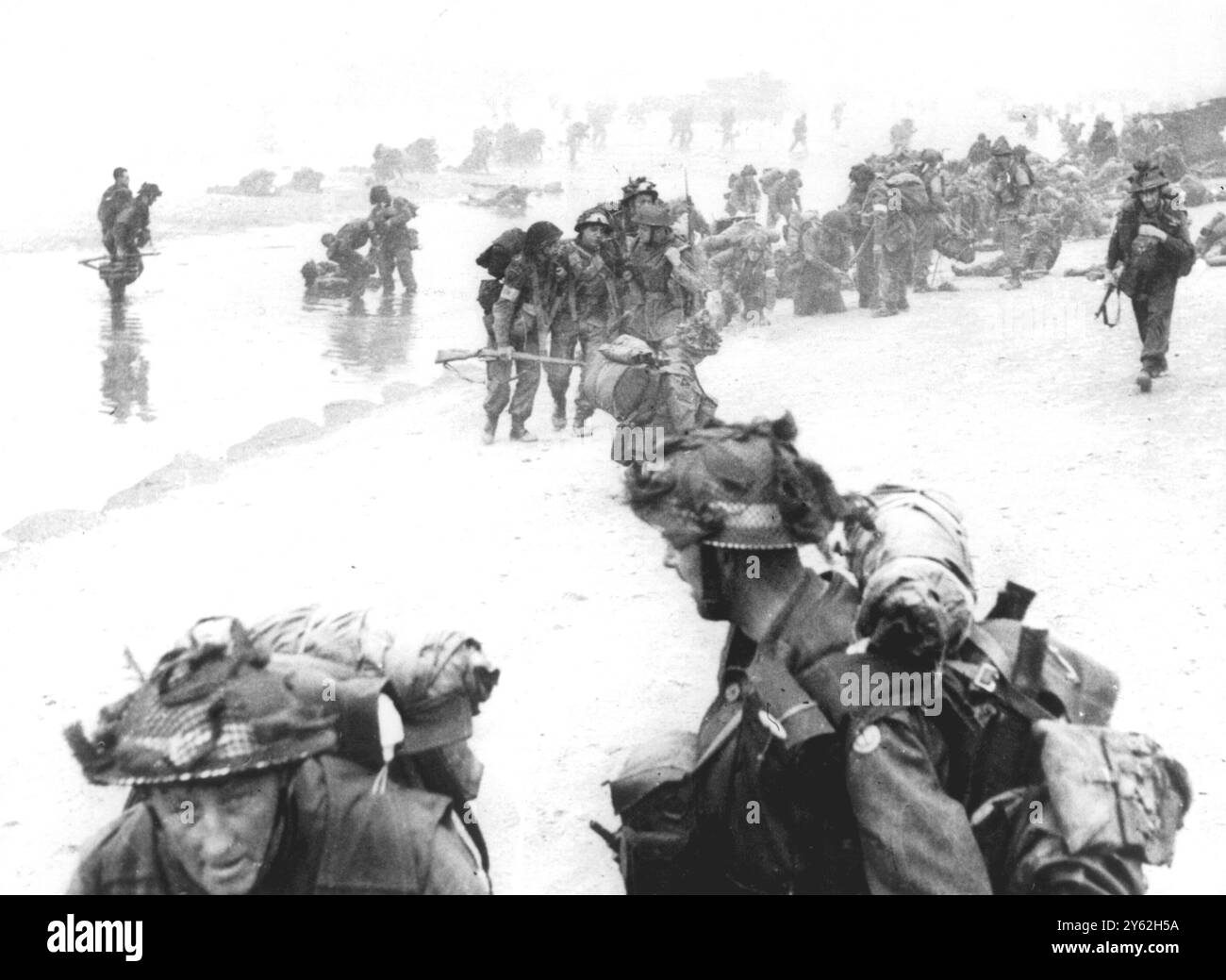 Normandie, Frankreich. D-Day Landungen. Britische Soldaten, viele von ihnen verletzt, landen am Sword Beach. 1944 'der Auslöser klickte um 8:32 Uhr, als Queen Red Beach nahe La Breche, Hermanville-sur-mer unter Granulat und Mörserfeuer geriet. Im Vordergrund und rechts befinden sich Spangen von 84 Royal Engineers der Field Company. Hinter ihnen bereiten sich schwer beladene Sanitäter von 8 Feldambulanten des Royal Army Medical Corps vor, von denen einige verwundete Männer behandeln, um den Strand zu verlassen. Im Hintergrund schwärmen Männer des 1. Bataillons, des Suffolk-Regiments und des No. 4 Army Commando von Landefahrzeugen an Land. Andere in Stockfoto