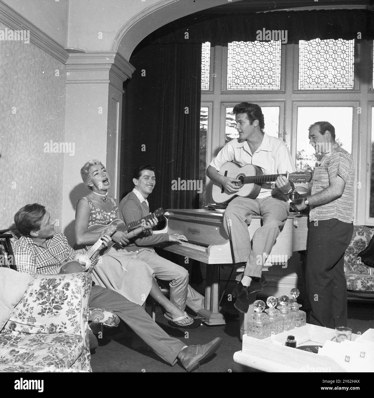 Roger Moore 1958. Im britischen Haus, das er mit seiner Frau Dorothy Squires teilte, The Mount, Wansunt Road, Bexleyheath. Piano-Spieler ist Tony Osborne, weit links Gary Miller (Sänger, großer Hit Robin Hood-Thema) ganz rechts Robert Brown, dann Squire Gurth in Ivanhoe mit Moore, später M in den James-Bond-Filmen von 1981. Stockfoto