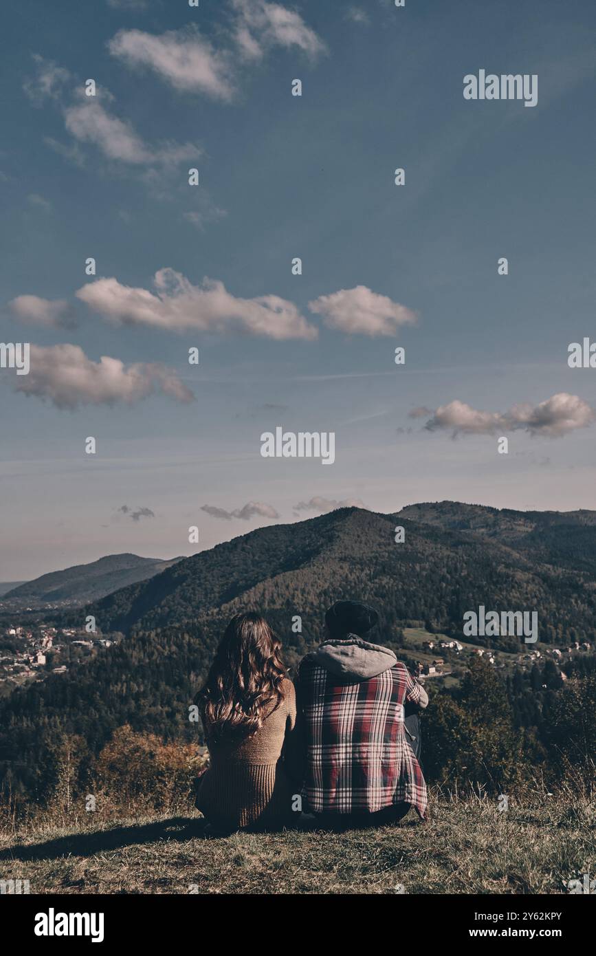 All die Sorgen sind weggeflogen... Rückansicht eines jungen Paares, das die Aussicht bewundert, während es auf dem Gipfel sitzt Stockfoto