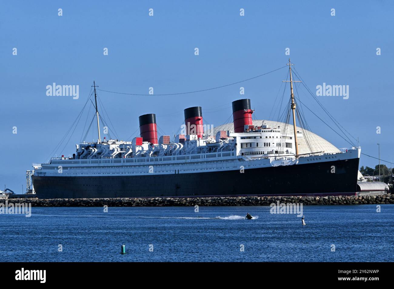 LONG BEACH, KALIFORNIEN - 19. SEPTEMBER 2024: The Queen Mary Hotel. Permanent im Hafen verankert, während ein Jet-Ski vorbeizieht. Stockfoto