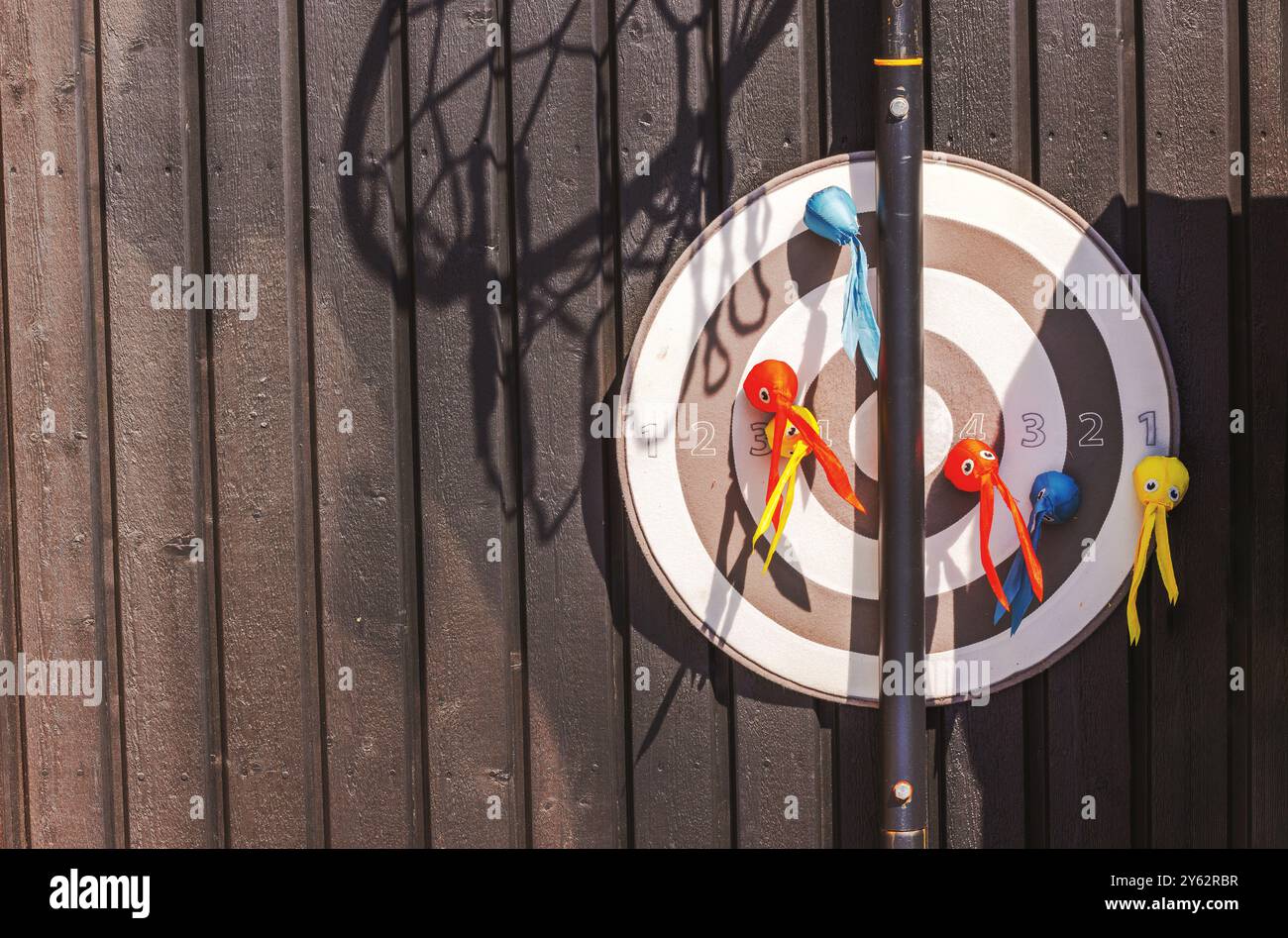 Nahaufnahme des spielerischen Zielspiels mit bunten Spielzeugen an Holzwand unter Sonnenlicht. Stockfoto