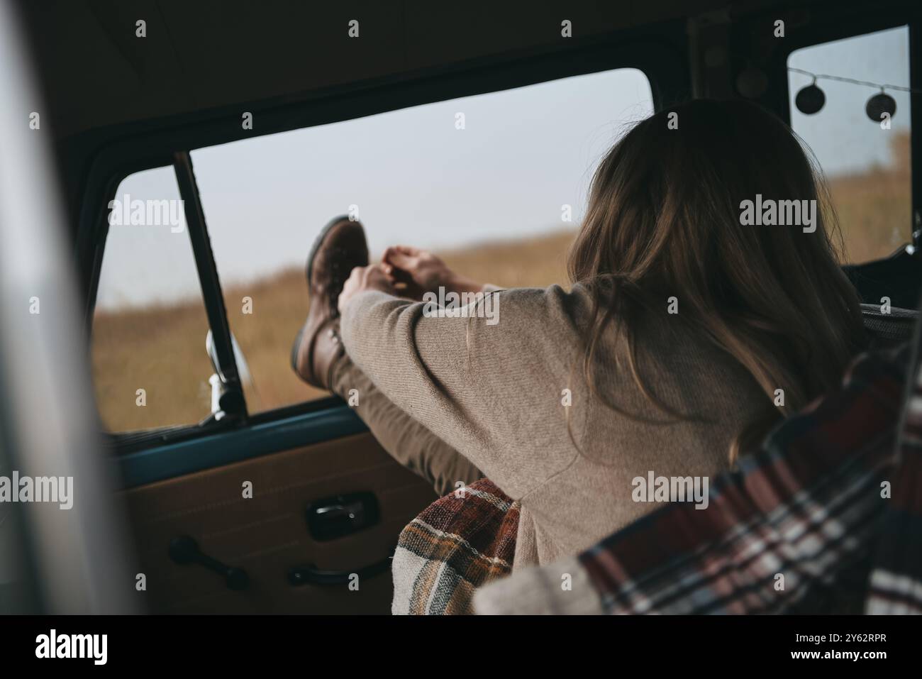 Angenehmer Roadtrip. Rückansicht einer jungen Frau, die sich beim Sitzen auf dem Beifahrersitz im Retro-Stil ausdehnt Stockfoto