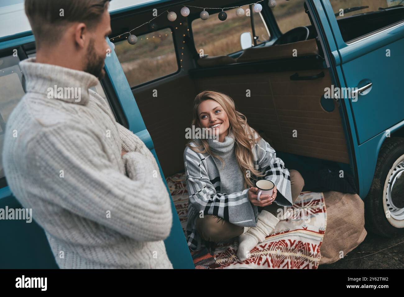 Lassen Sie all Ihre Sorgen hinter sich! Schöne junge Frau, die ihren Freund ansieht und lächelt, während sie in einem blauen Minibus im Retro-Stil sitzt Stockfoto