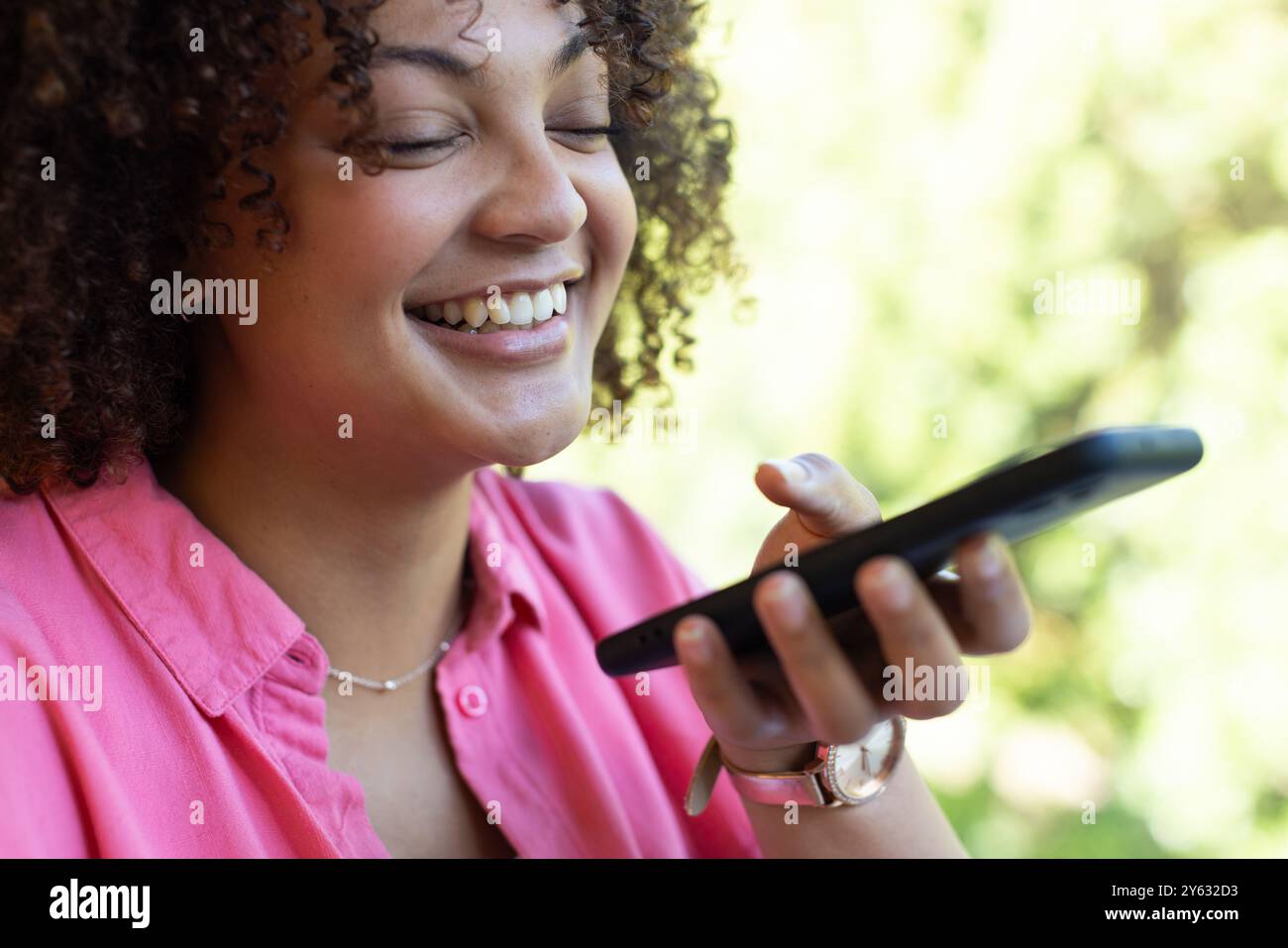 Lächelnde Frau, die das Smartphone für Sprachnachrichten nutzt, im Freien Gespräche genießt, zu Hause Stockfoto