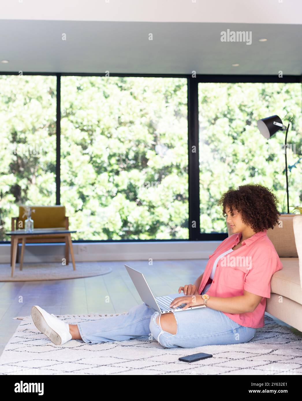 Auf dem Boden sitzend, Frau mit Laptop und Smartphone im modernen Wohnzimmer, Kopierraum, zu Hause Stockfoto