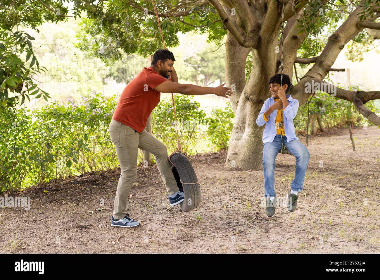 Der Sohn wird auf die Reifenschaukel geschoben, der indische Vater genießt gemeinsam Outdoor-Spielzeit Stockfoto