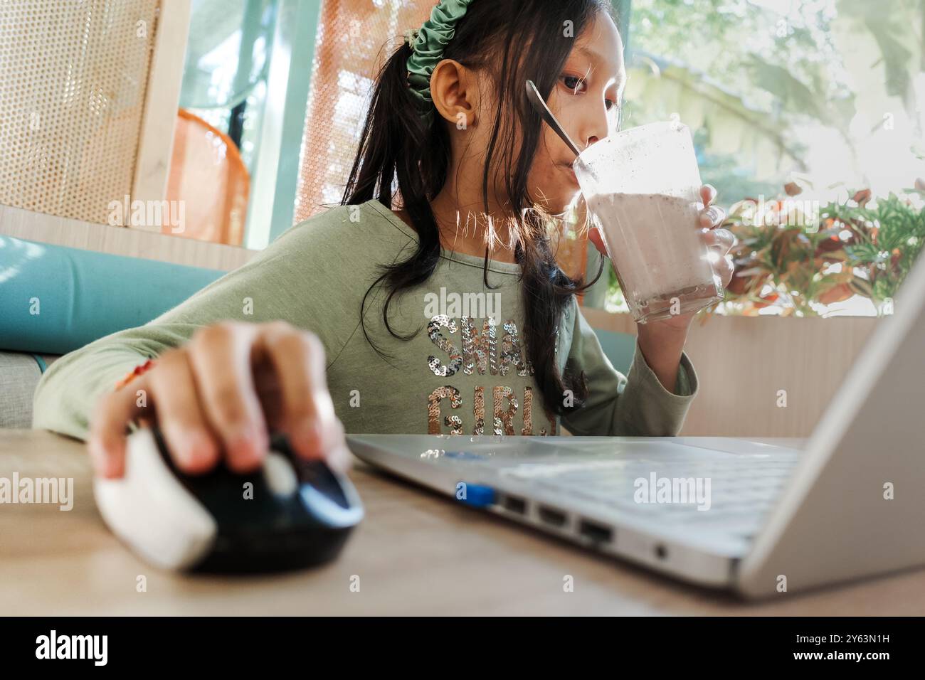 Südostasiatische Teenagerin trinkt, während sie in einem Restaurant einen Laptop benutzt Stockfoto