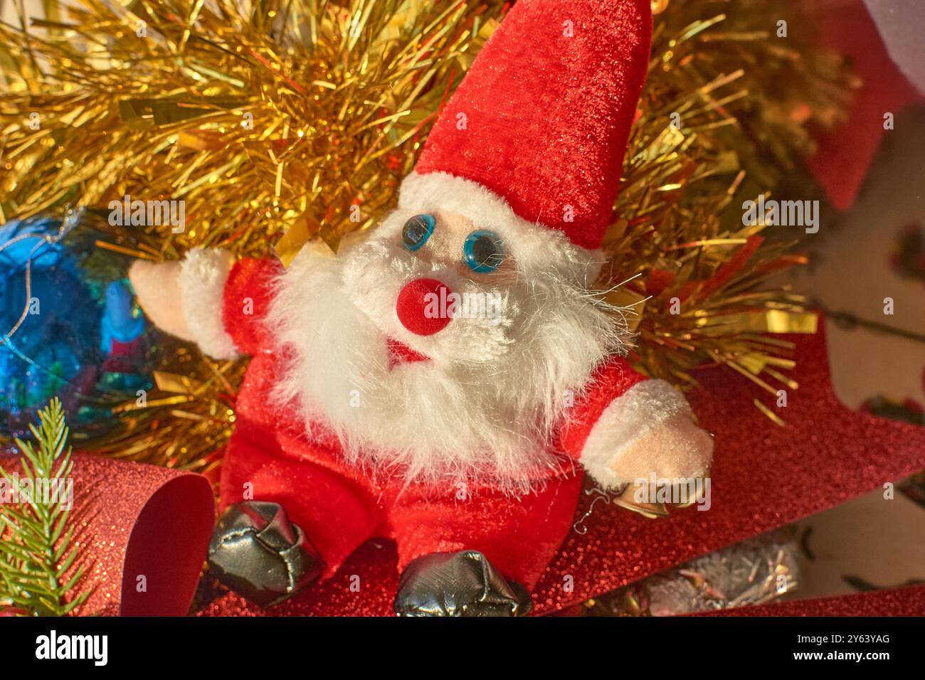 Plüschtier des Weihnachtsmanns, das in einer festlichen Weihnachtsszene sitzt. Die Weihnachtsmannfigur mit ihrem flauschigen weißen Bart, dem hellroten Anzug und den blauen Augen ist surr Stockfoto