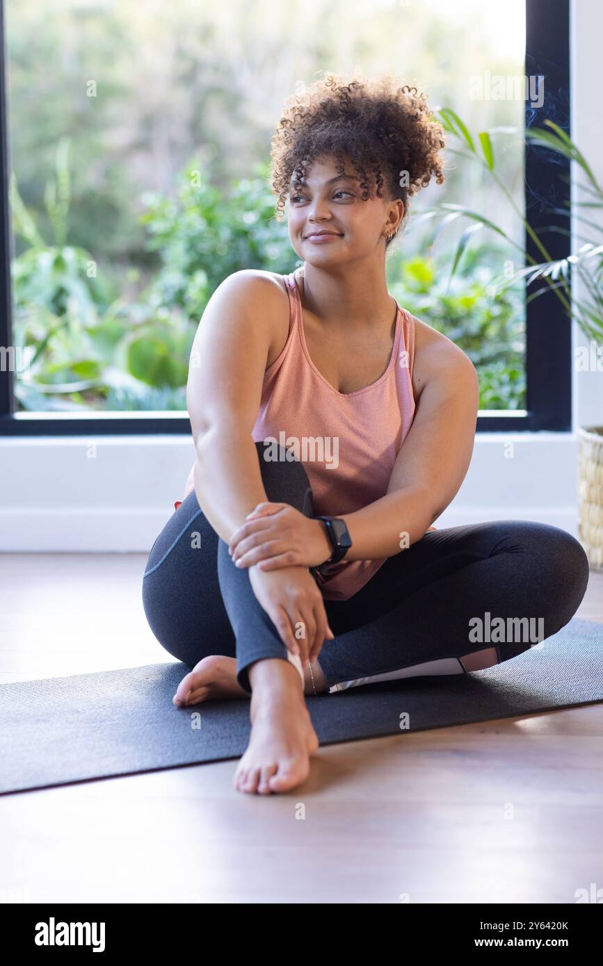 Sitzend auf Yogamatte, plus große Frau lächelt und dehnt sich im Fitnessstudio, zu Hause, zu Hause Stockfoto