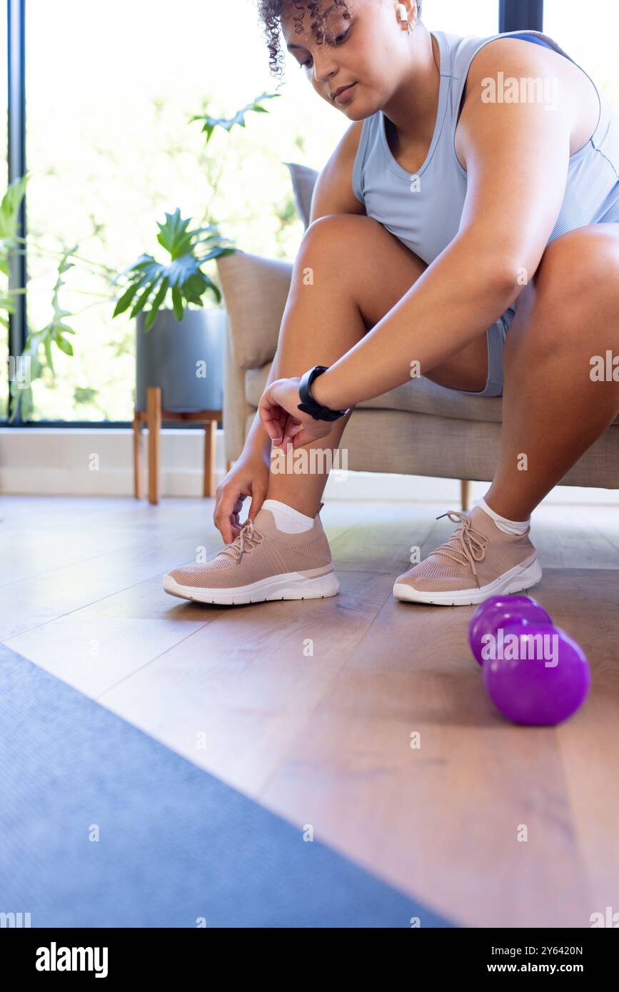 Schnürsenkel binden und große Frau, die sich auf das Training vorbereitet, mit Kurzhanteln in der Nähe, zu Hause, zu Hause Stockfoto