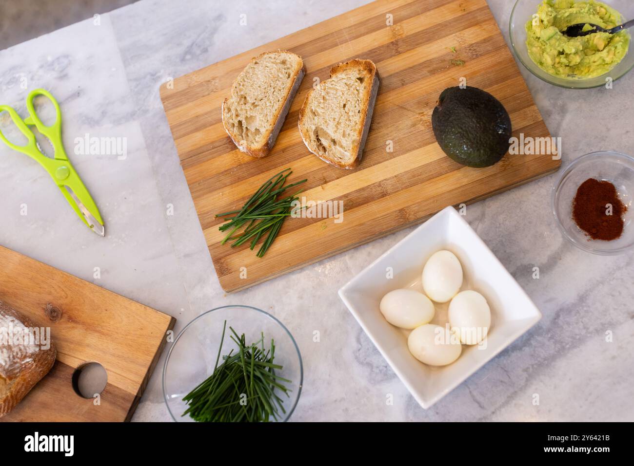 Zubereitung von Avocadotoast, Brotscheiben, gekochten Eiern und Schnittlauch auf Schneidebrett, zu Hause, zu Hause Stockfoto
