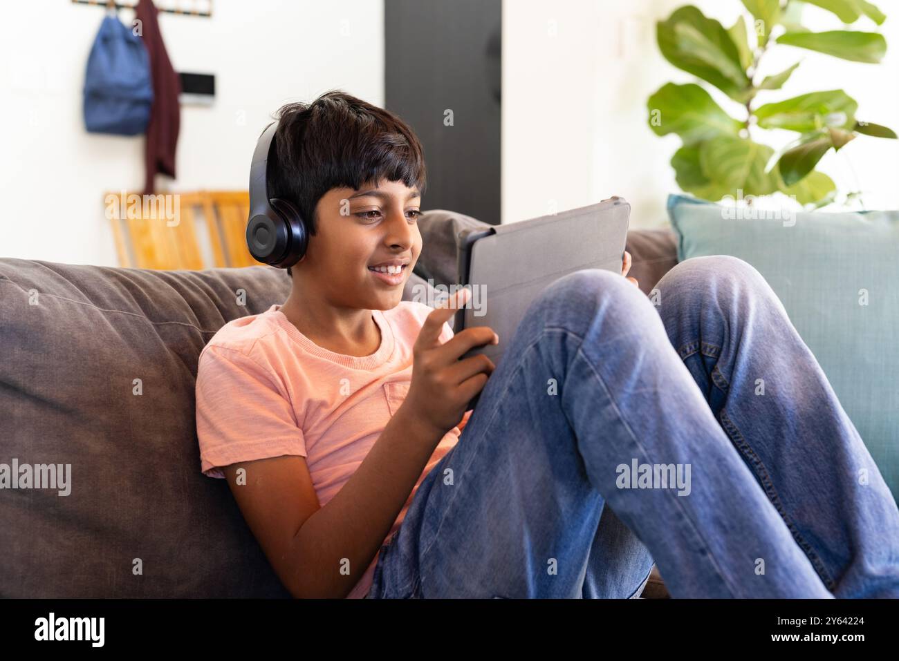 Mit Kopfhörern, Indianerjunge sitzt auf der Couch und lächelt Stockfoto