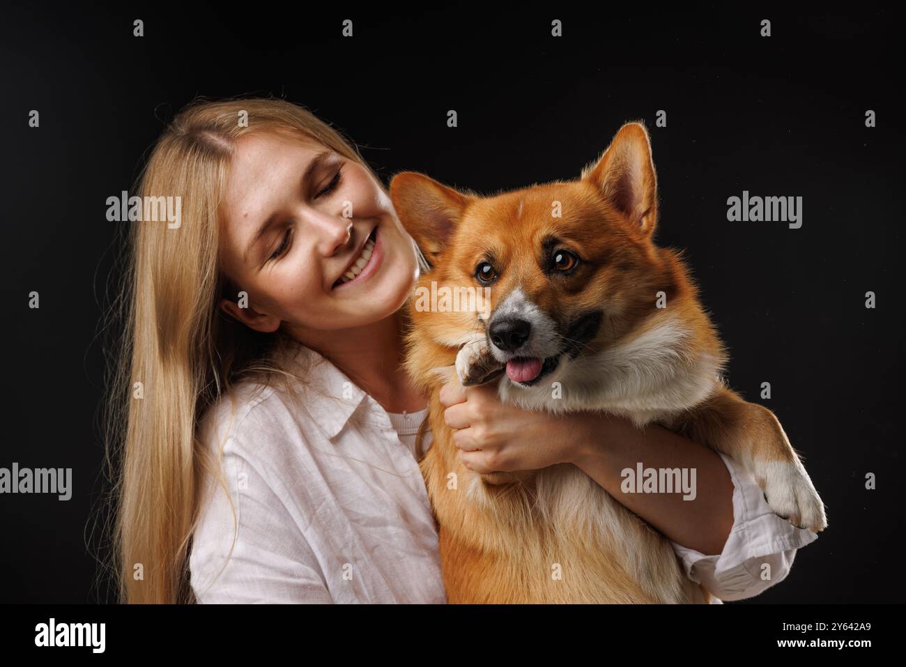 Frau, die einen glücklichen Corgi-Hund auf schwarzem Hintergrund hält und umarmt. Elegantes Konzept. Liebe Hunde Stockfoto
